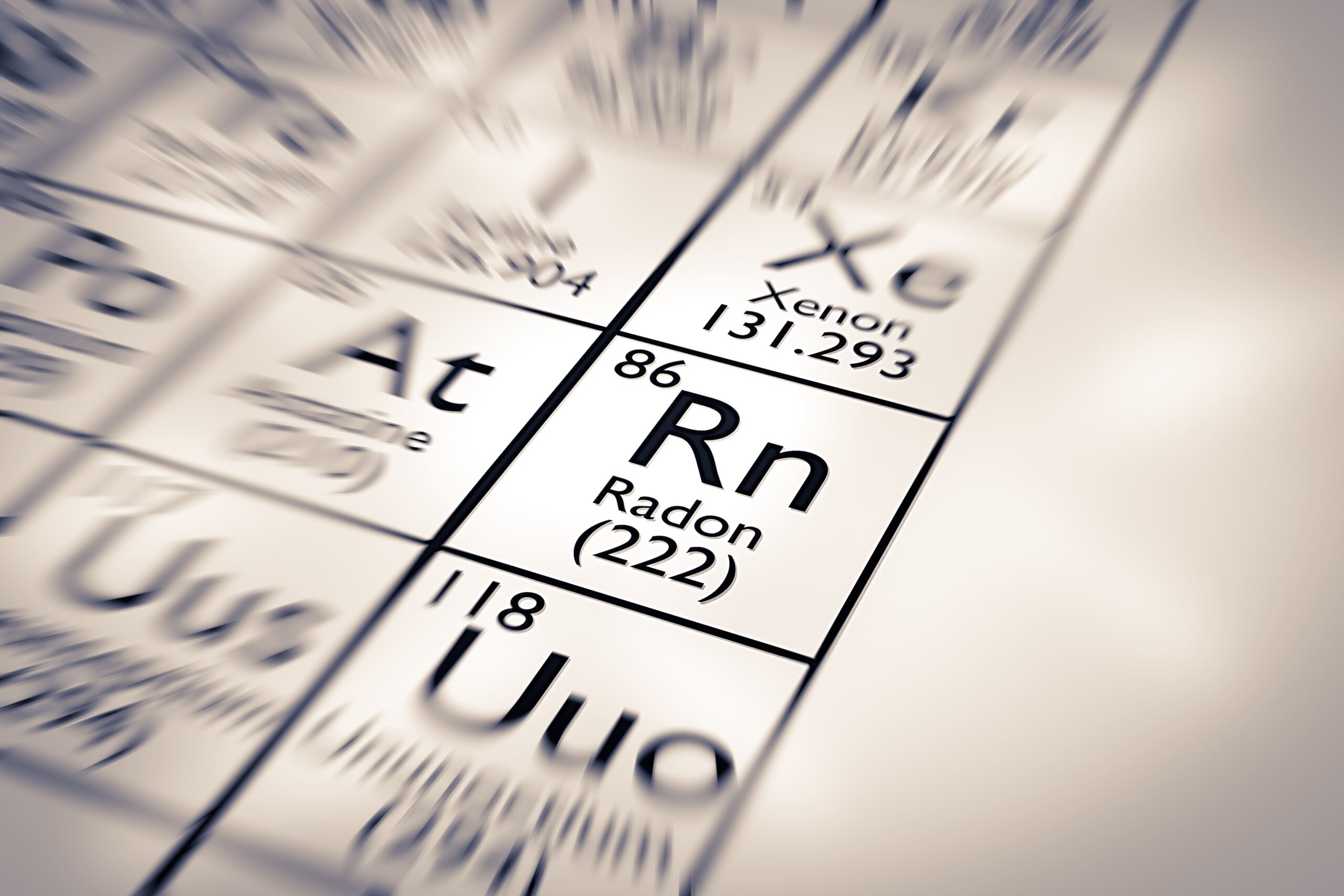Ein Bildausschnitt der Periodentabelle, fokussiert auf das Element Radon (Rn, Ordnungszahl 86) mit der Angabe der Atommasse (≈222). Andere Elemente wie Xenon (Xe) und Astat (At) sind unscharf im Hintergrund zu sehen.