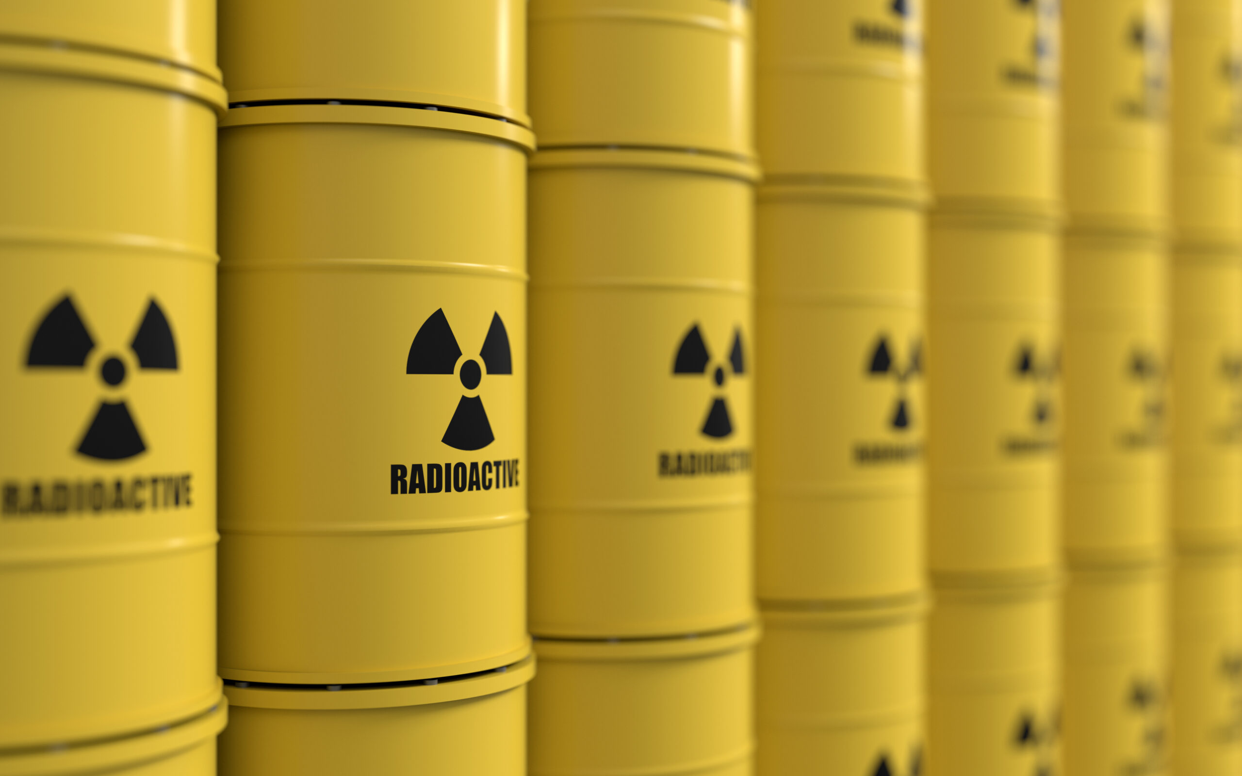 Gelbe Metallfässer mit Warnsymbolen für Radioaktivität, im Hintergrund eine Reihe weiterer Fässer.
